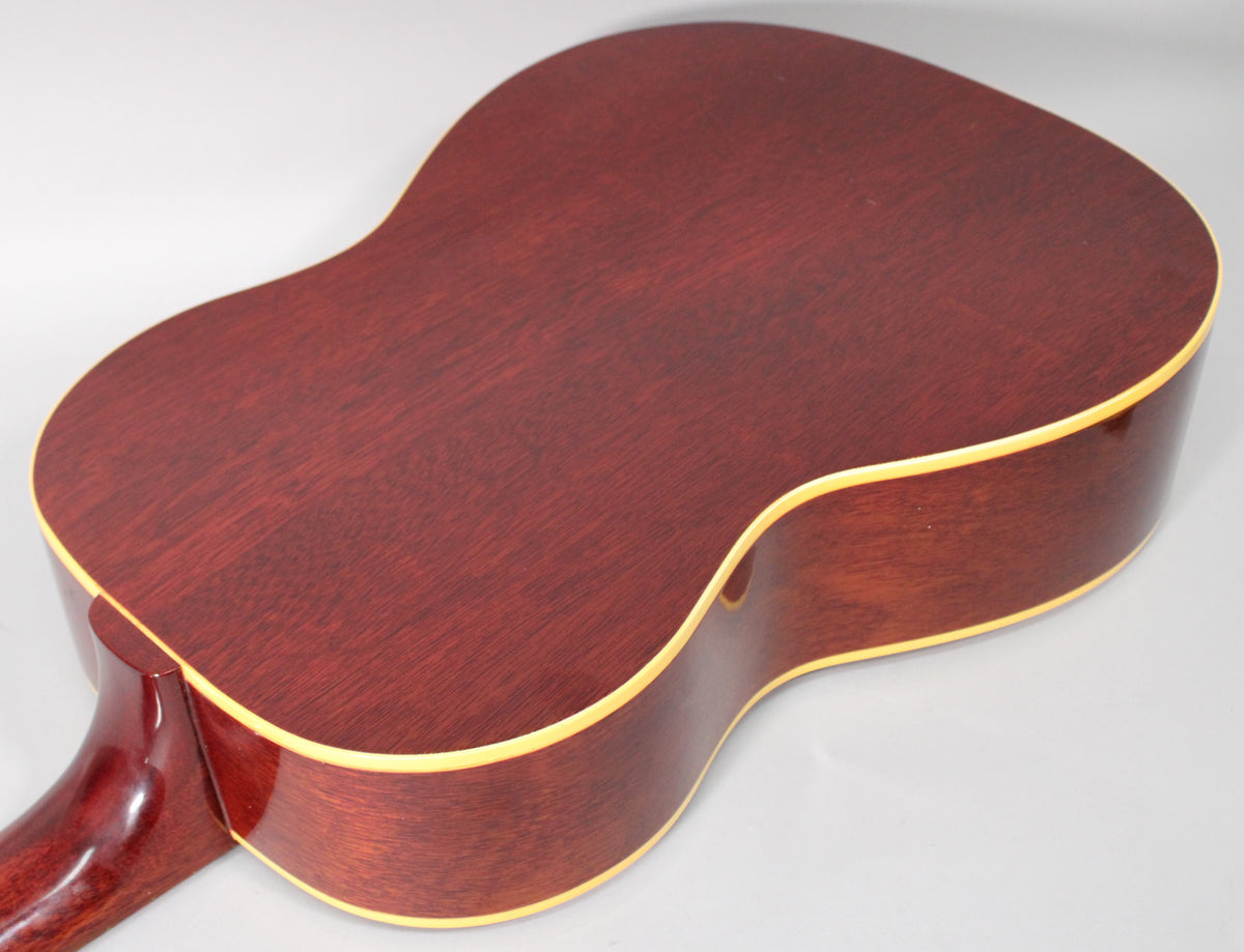 The guitar's dark reddish-brown back and sides are visible from the upper bout, with cream binding and a glossy neck heel.