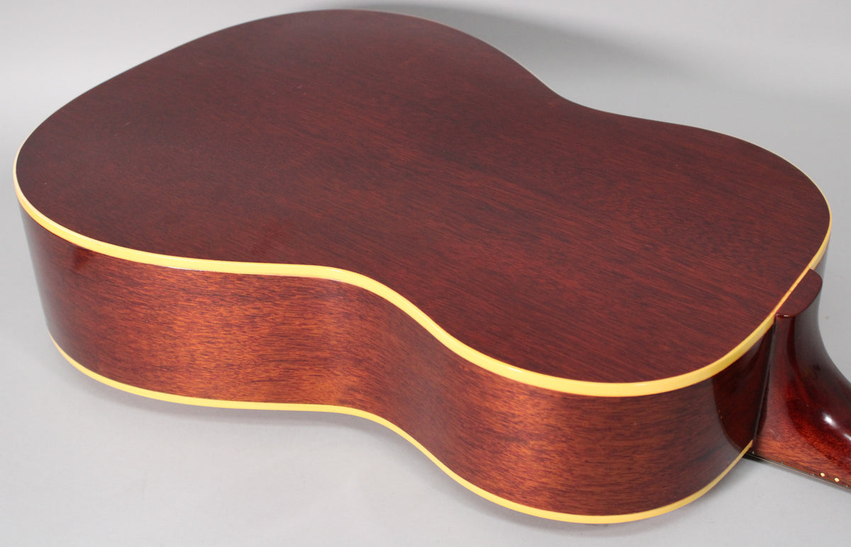 The guitar's dark reddish-brown back and sides, with a subtle wood grain, are framed from the lower bout, showing light binding.
