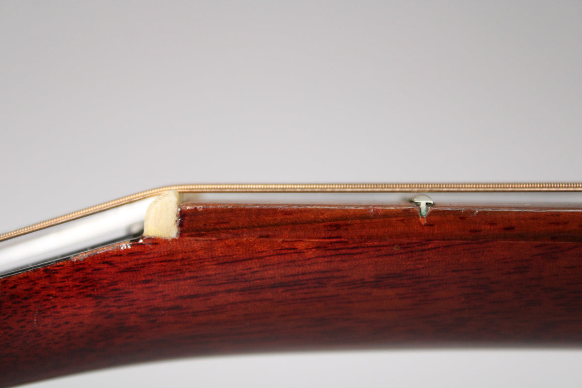 Close-up of the guitar's dark reddish-brown neck and fretboard, showing a white nut, a string tree, and some finish wear.