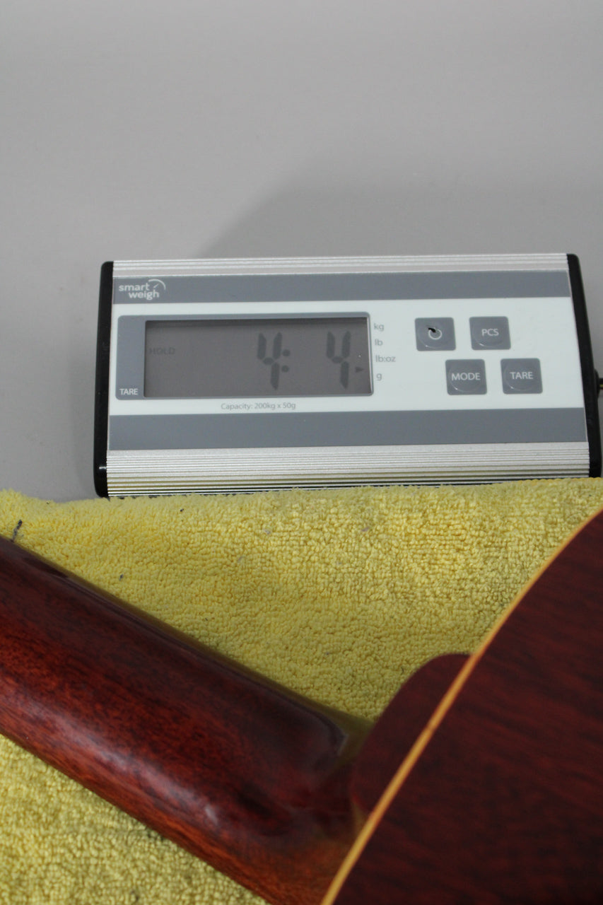 The guitar's dark reddish-brown neck and body are partially visible, resting on a yellow towel beneath a digital scale displaying "4.4".