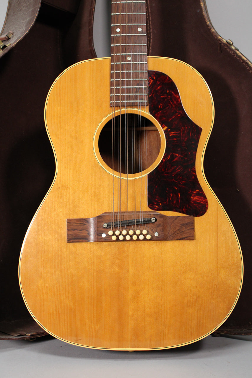 The 12-string acoustic guitar, with a natural finish, is framed from the neck to the bottom, showing a dark tortoiseshell pickguard.