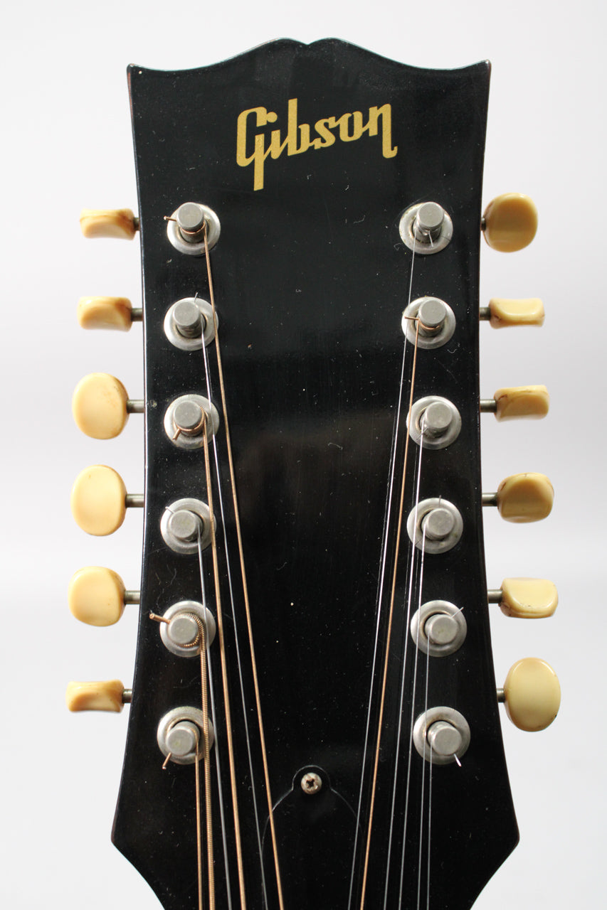 Close-up of the guitar's black headstock, showing 12 cream-colored tuning pegs and strings, with some finish wear.