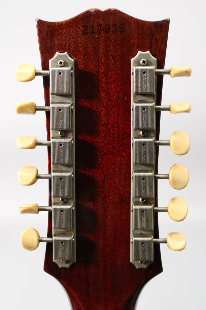 The guitar's dark reddish-brown headstock, with a worn top edge, shows 12 cream tuning pegs on two chrome strips.