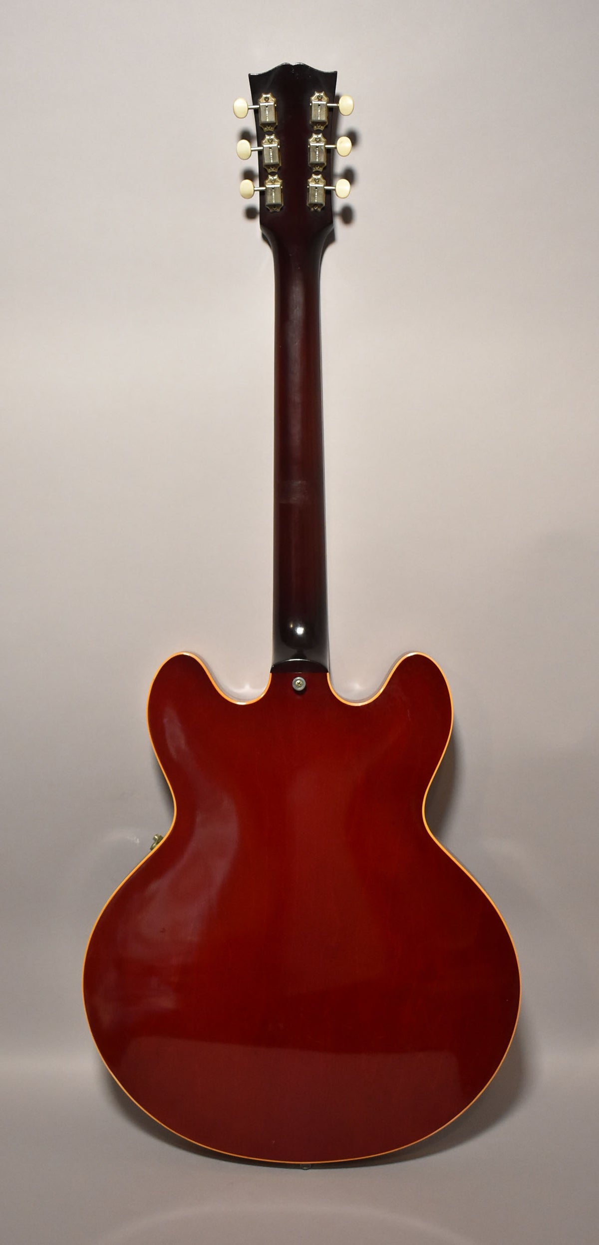 The guitar's cherry red back, neck, and headstock are visible, with six cream tuning pegs and some finish wear on the neck.