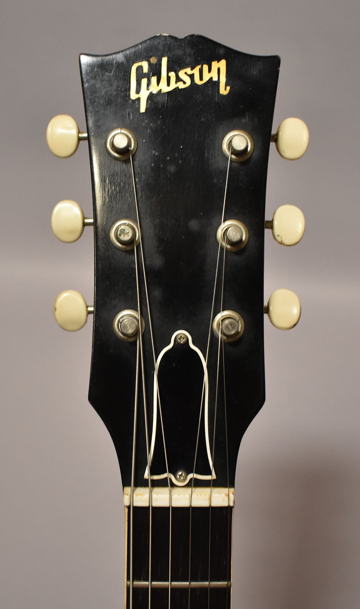 Close-up of the black headstock with gold Gibson logo, six cream tuning pegs, and a bell-shaped truss rod cover.