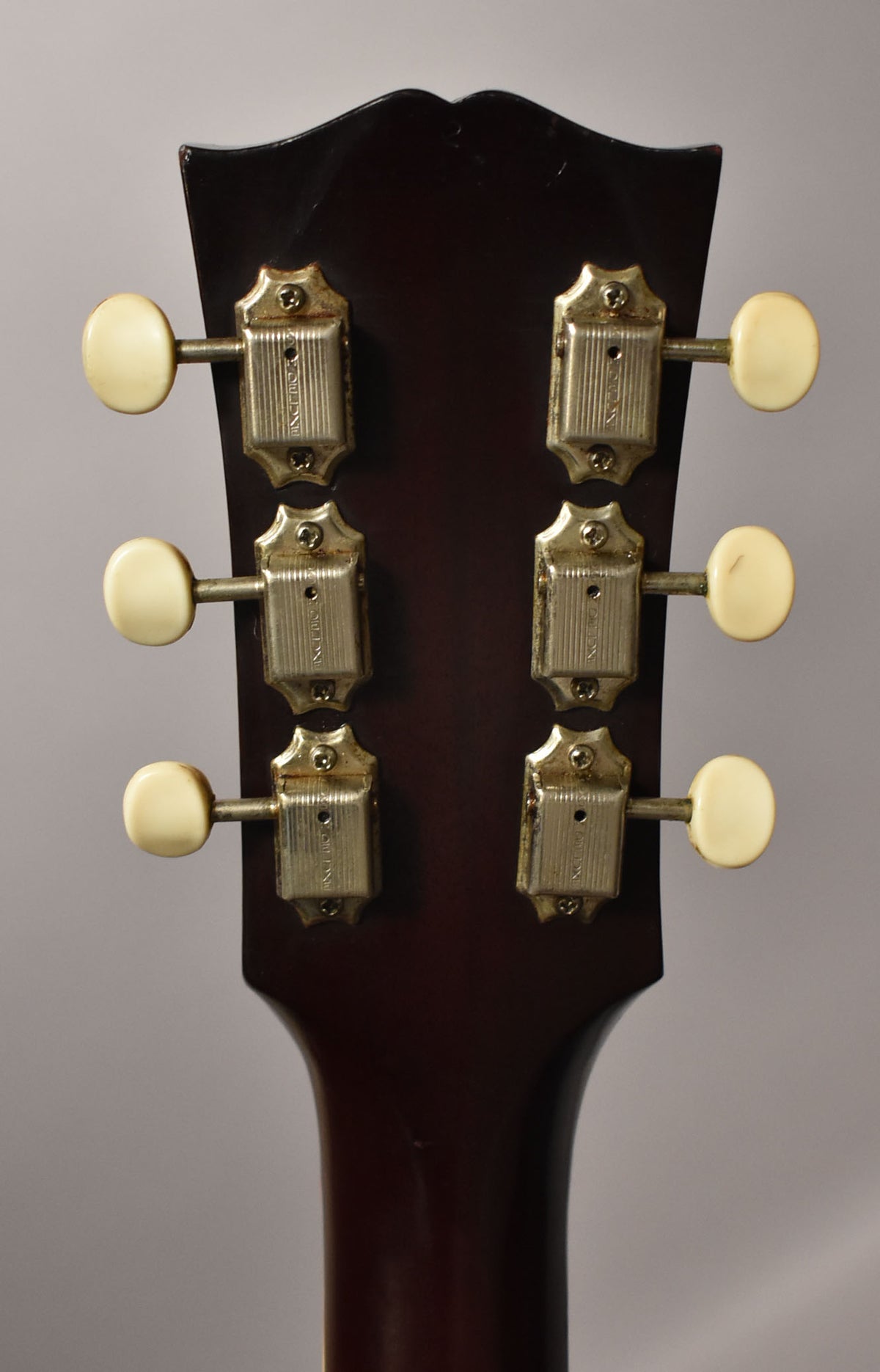 Rear view of the dark cherry headstock and neck, showing six cream-buttoned tuners with tarnished metal housings.