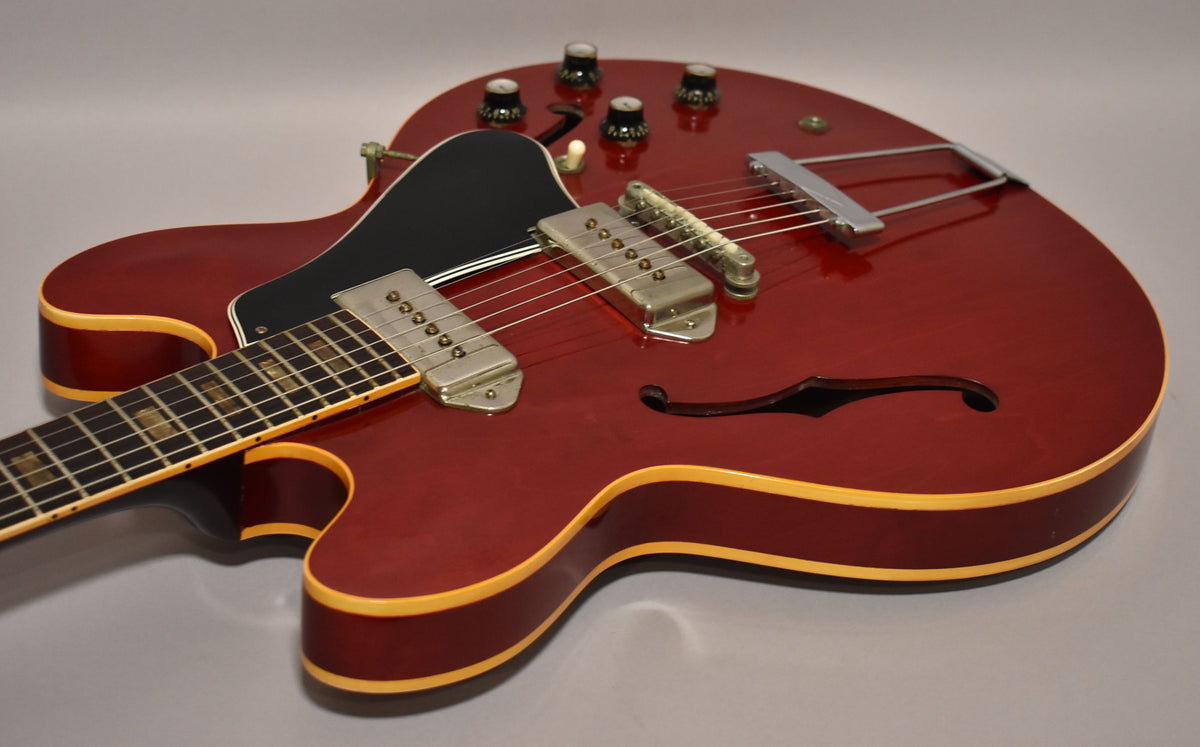 Cherry red hollowbody guitar, angled from the lower bout, showing two P90 pickups, four knobs, and a trapeze tailpiece.