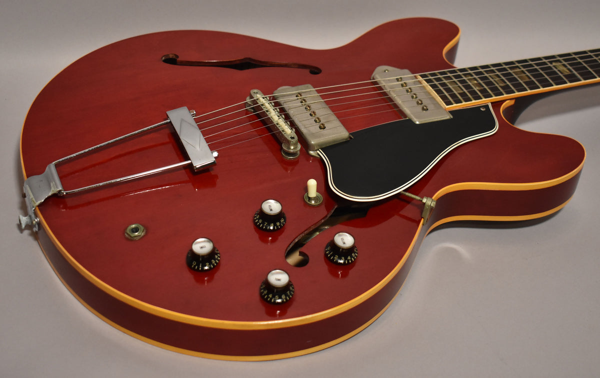 Cherry red hollowbody electric guitar, angled from the lower bout, showing two P90 pickups, black pickguard, and four control knobs.