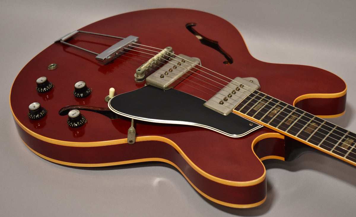Cherry red hollowbody guitar, angled from the lower bout, showing four black knobs, two P90 pickups, and a black pickguard.