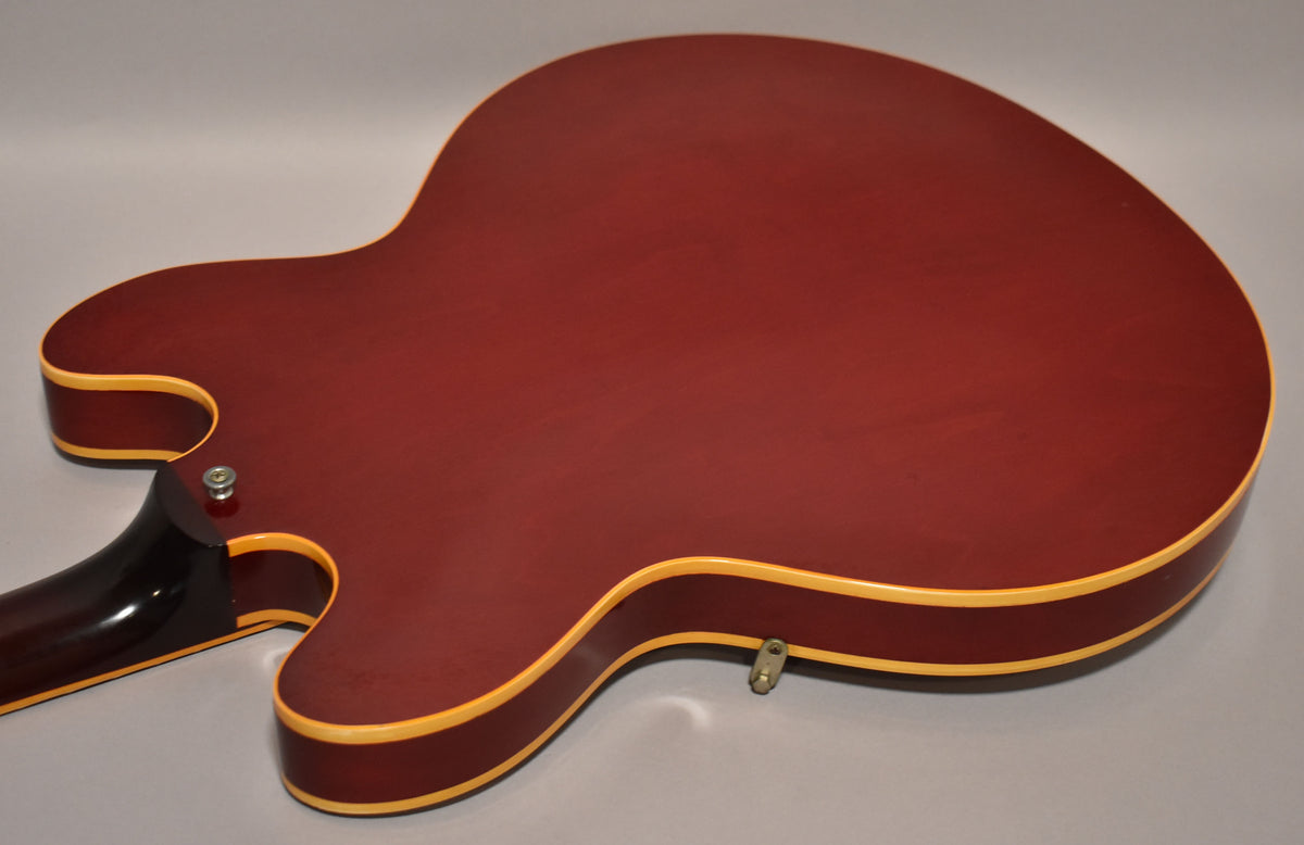 The cherry red hollowbody guitar's back is shown, revealing light finish wear, cream binding, and a chrome strap button.