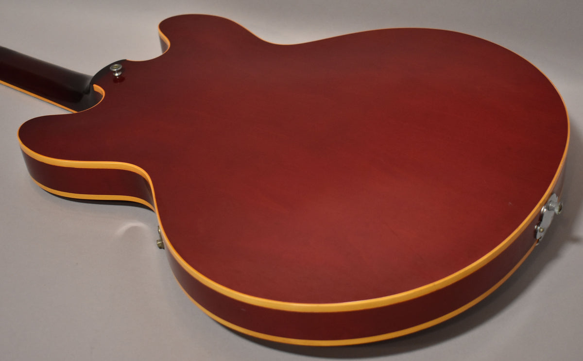 The cherry red hollowbody guitar's back is angled, showing light finish wear and cream binding along the edges.
