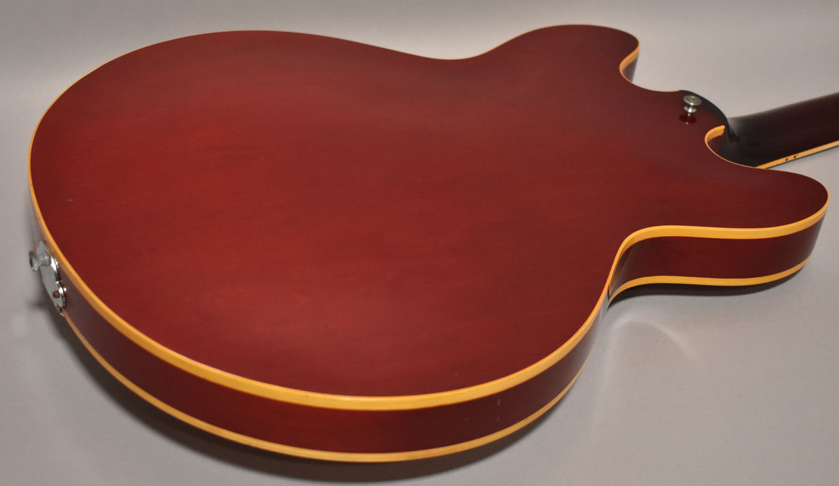 The cherry red hollowbody guitar's back is visible, showing light finish wear, cream binding, and a chrome strap button.
