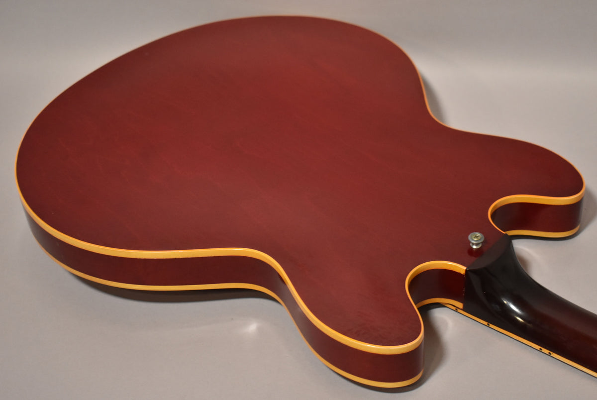The cherry red hollowbody guitar's back, showing light finish wear, cream binding, and the neck heel with a strap button.