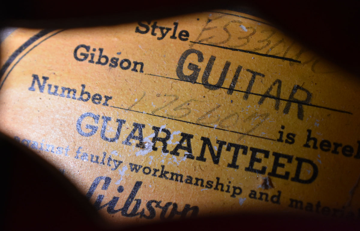 Close-up of the guitar's orange interior label, showing "Gibson GUITAR" and "GUARANTEED" with handwritten details and wear.
