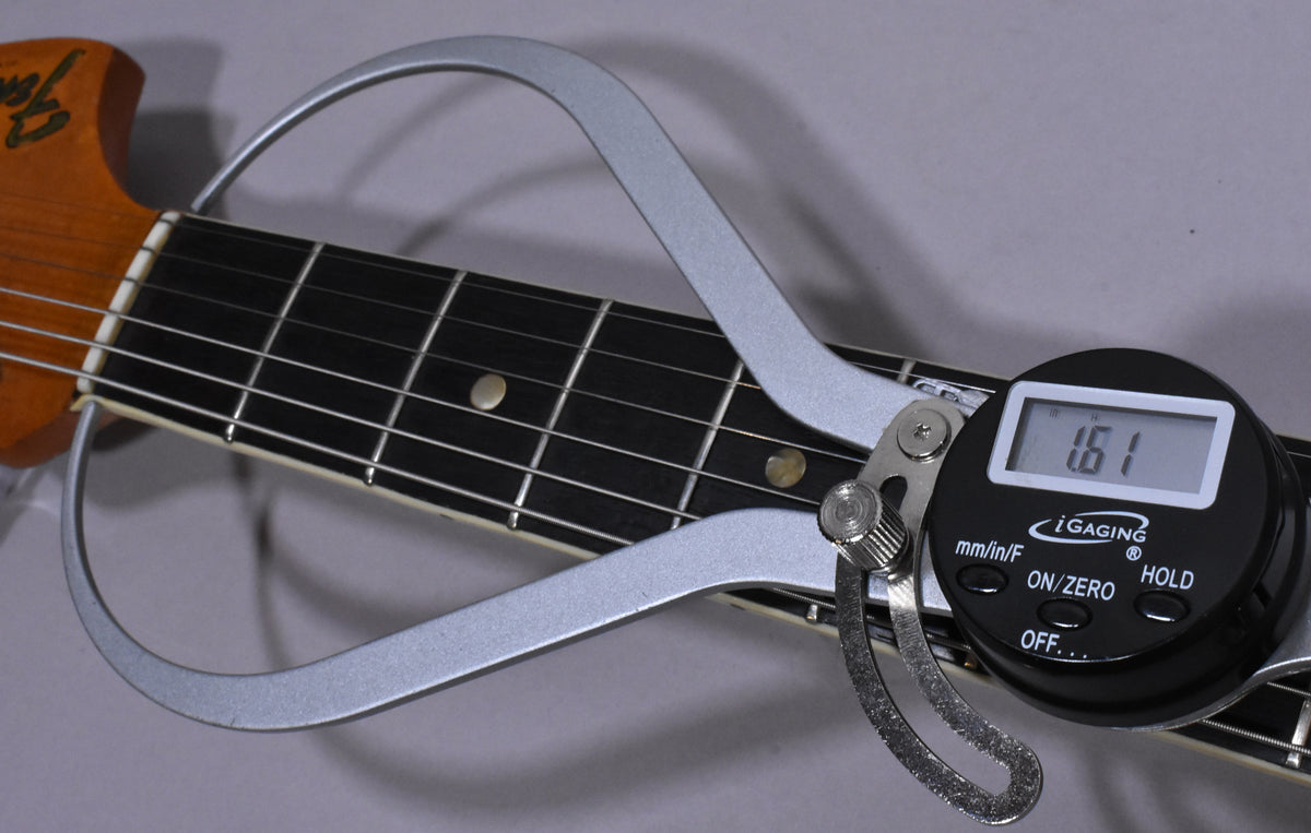 Close-up of the guitar's dark fretboard and light headstock, with a digital caliper measuring the nut width at 1.61 inches.