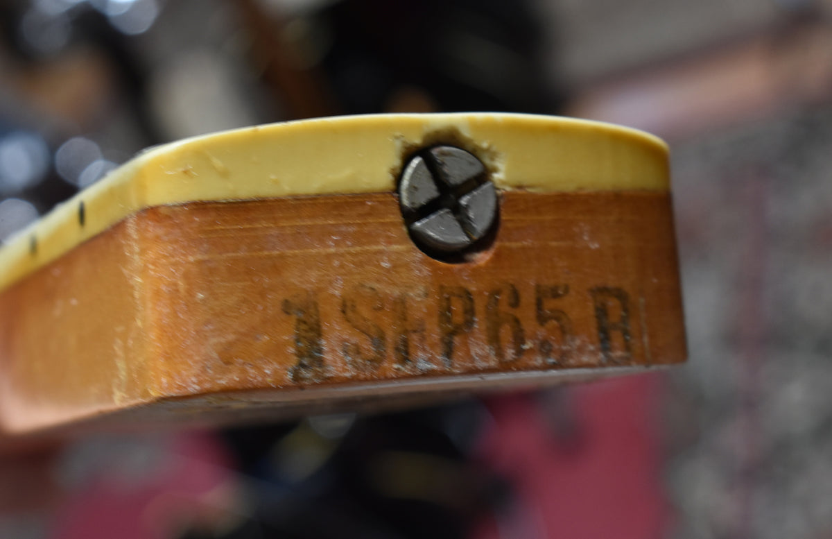 Close-up of the guitar neck heel, showing the light-colored fretboard overhang, a neck screw, and a faded "1965" stamp.