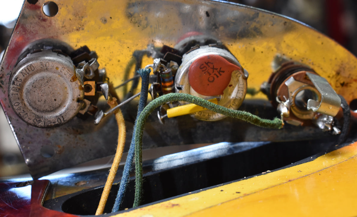 Close-up of the guitar's wiring cavity, revealing two pots, an orange capacitor, and the output jack with cloth-covered wires.