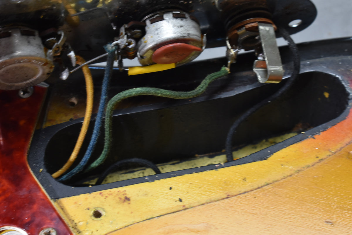 Close-up of the guitar's wiring cavity, showing vintage-style cloth-covered wires, solder joints, and the sunburst finish's yellow center.