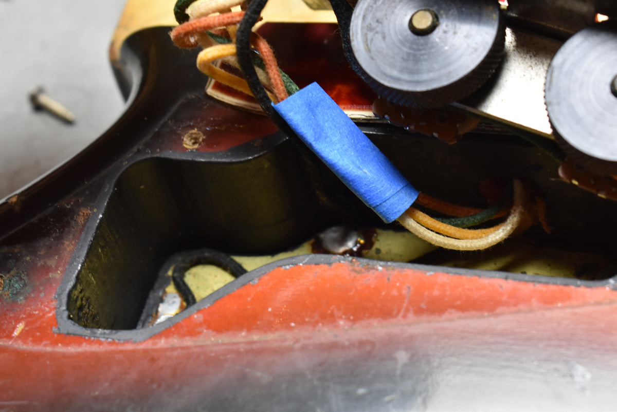 Close-up of the guitar's wiring cavity, showing a blue capacitor, cloth-covered wires, and worn sunburst finish with exposed wood.