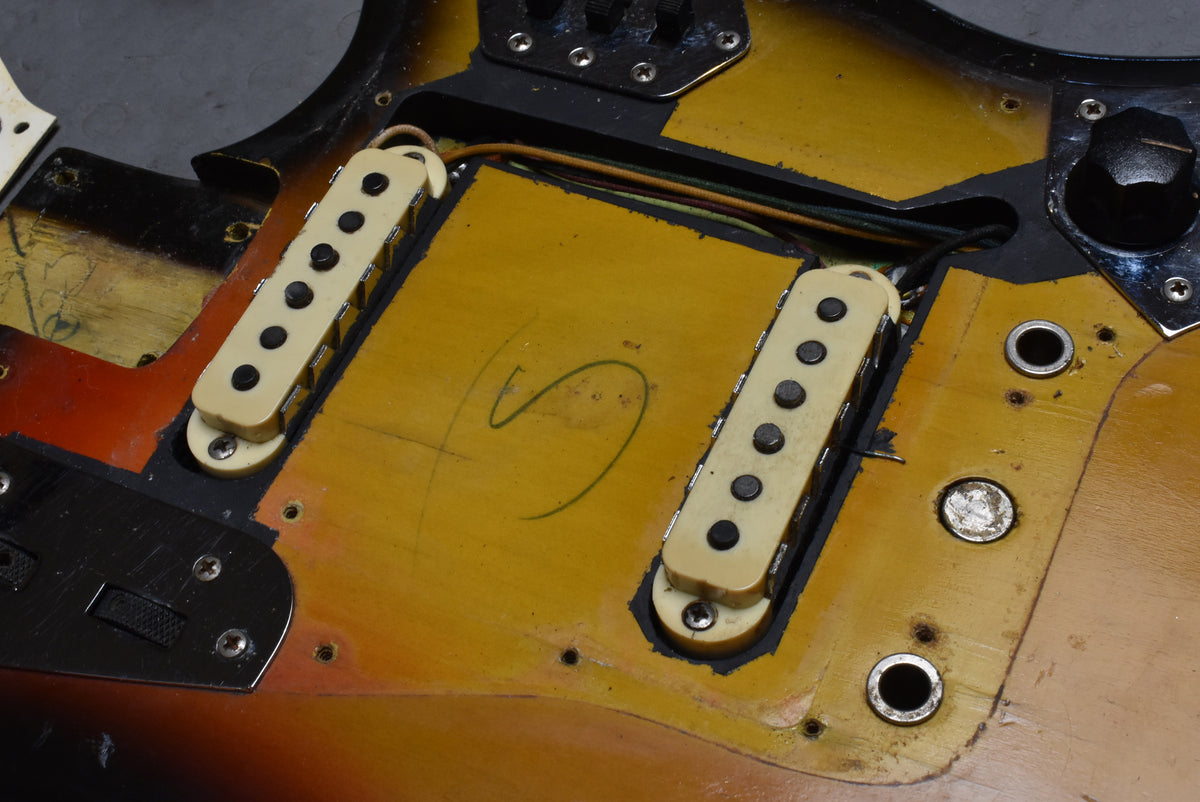 Close-up of the guitar body's sunburst finish, showing two cream single-coil pickups, control cavity, and a black roller switch plate.