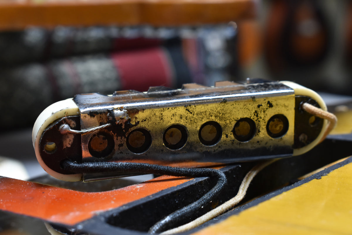 Close-up of a pickup with a tarnished chrome cover, cream bobbin ends, and visible wiring, resting on the sunburst body.