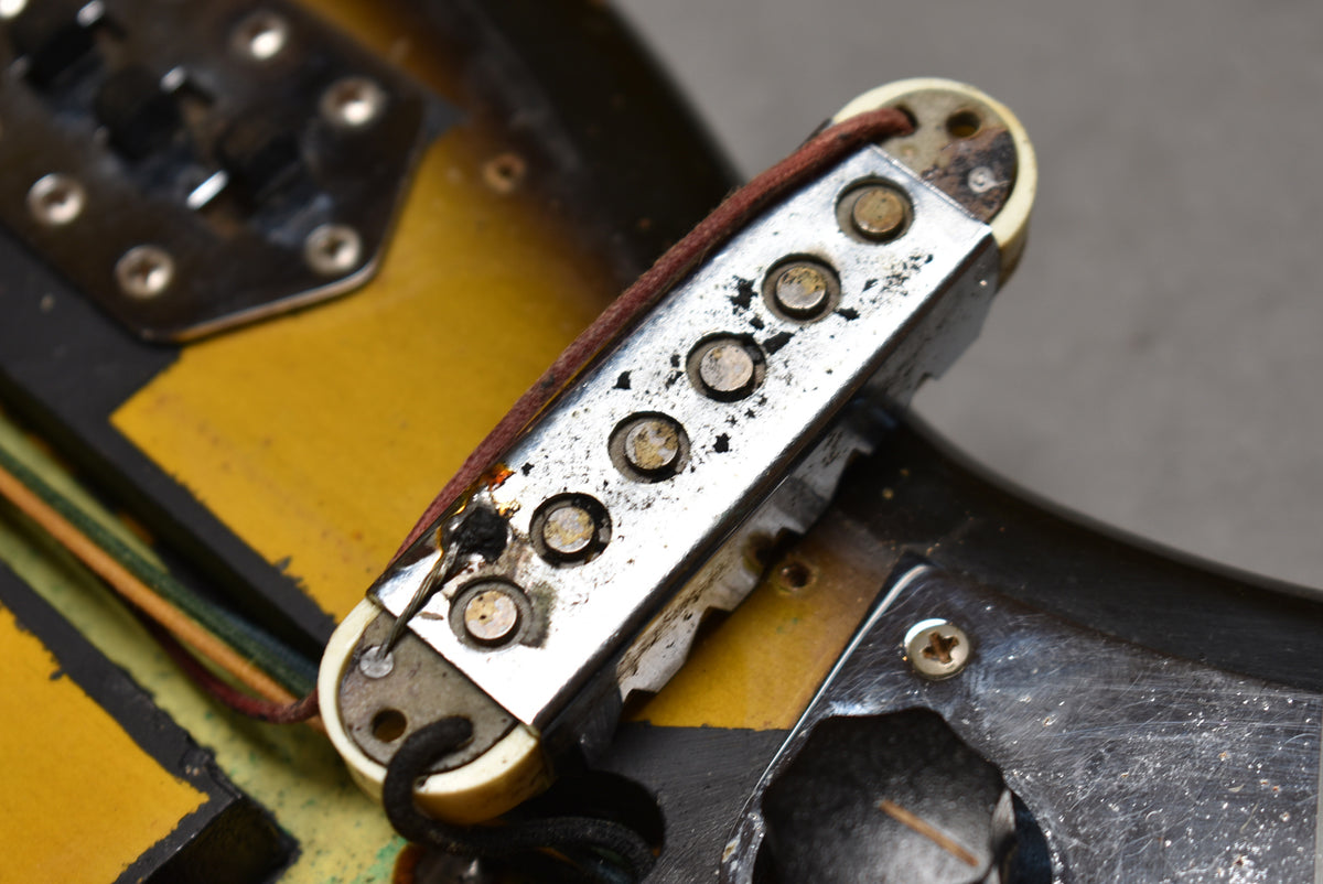 Close-up of a well-worn single-coil pickup with a tarnished chrome cover, showing exposed wiring and a cream bobbin.
