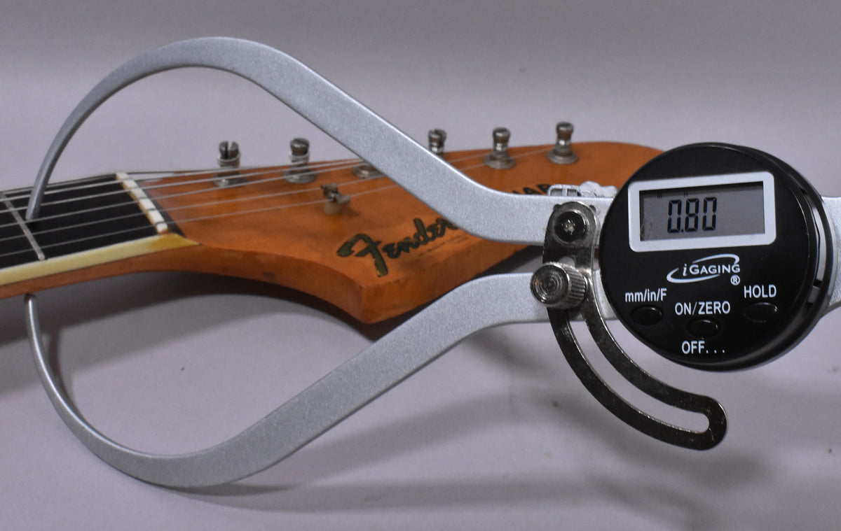 A digital caliper measures the neck thickness at the first fret, showing 0.80, with the headstock and tuners visible.