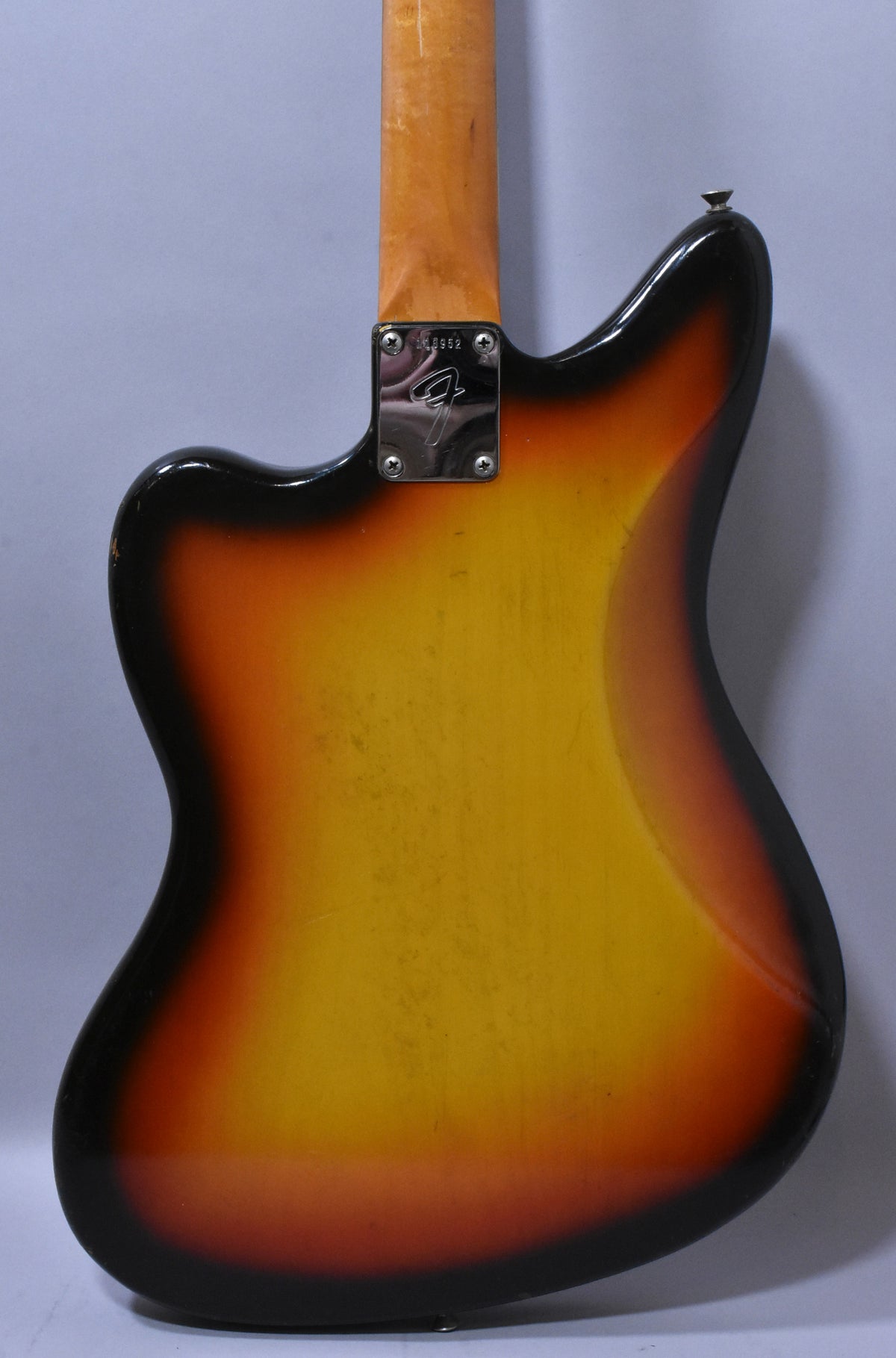 The back of a sunburst guitar body, showing a chrome neck plate, a strap button, and visible wear and scratches.