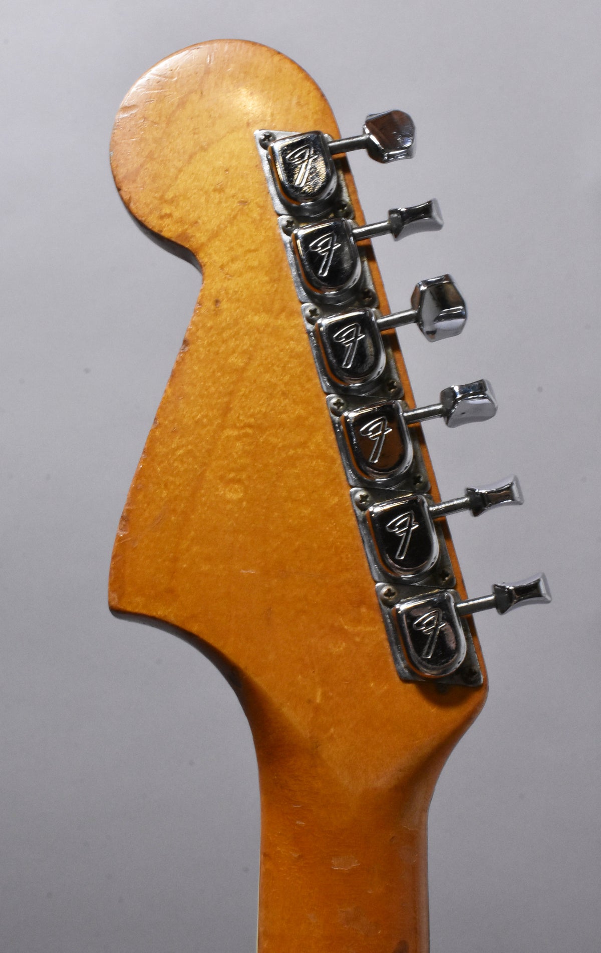 Close-up of the headstock, angled to show the six chrome tuners on the right, with visible wear and checking on the amber finish.