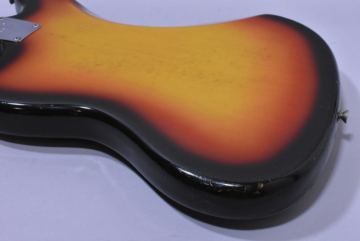 The back of a sunburst guitar body, showing wear and chips along the black edge, with a strap button visible on the lower bout.