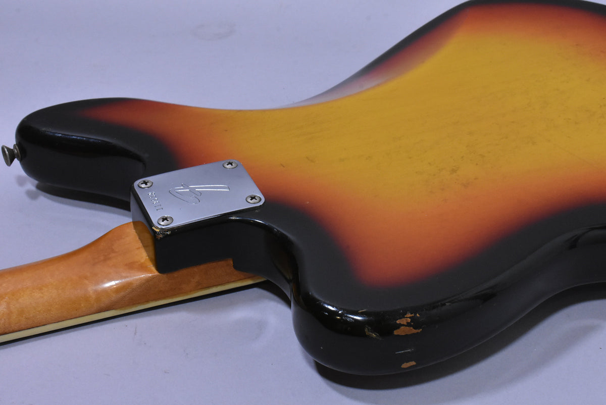 The guitar's sunburst body, with visible finish wear and checking, meets a light-colored neck with a chrome neck plate.