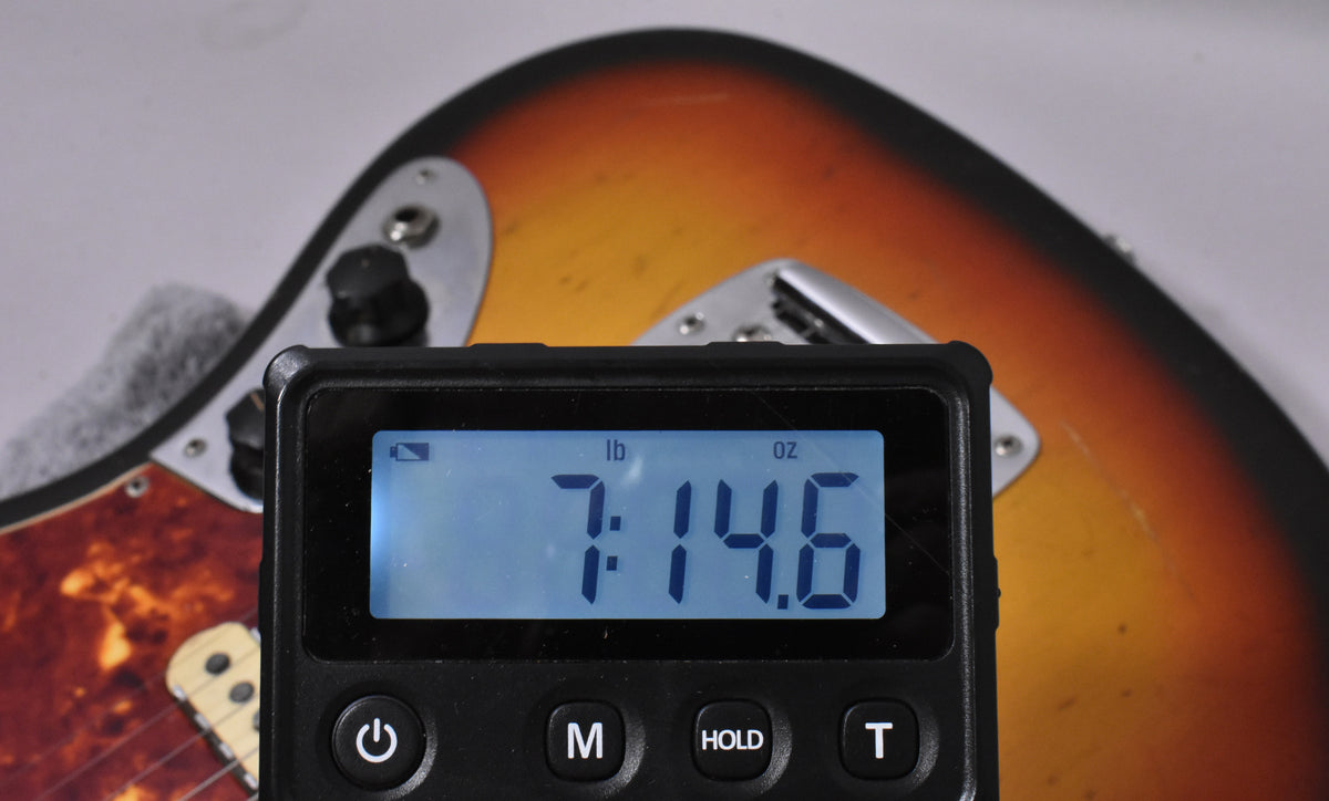 A digital scale displays "7:14.6 lb oz" over the sunburst body and tortoise pickguard of the guitar.