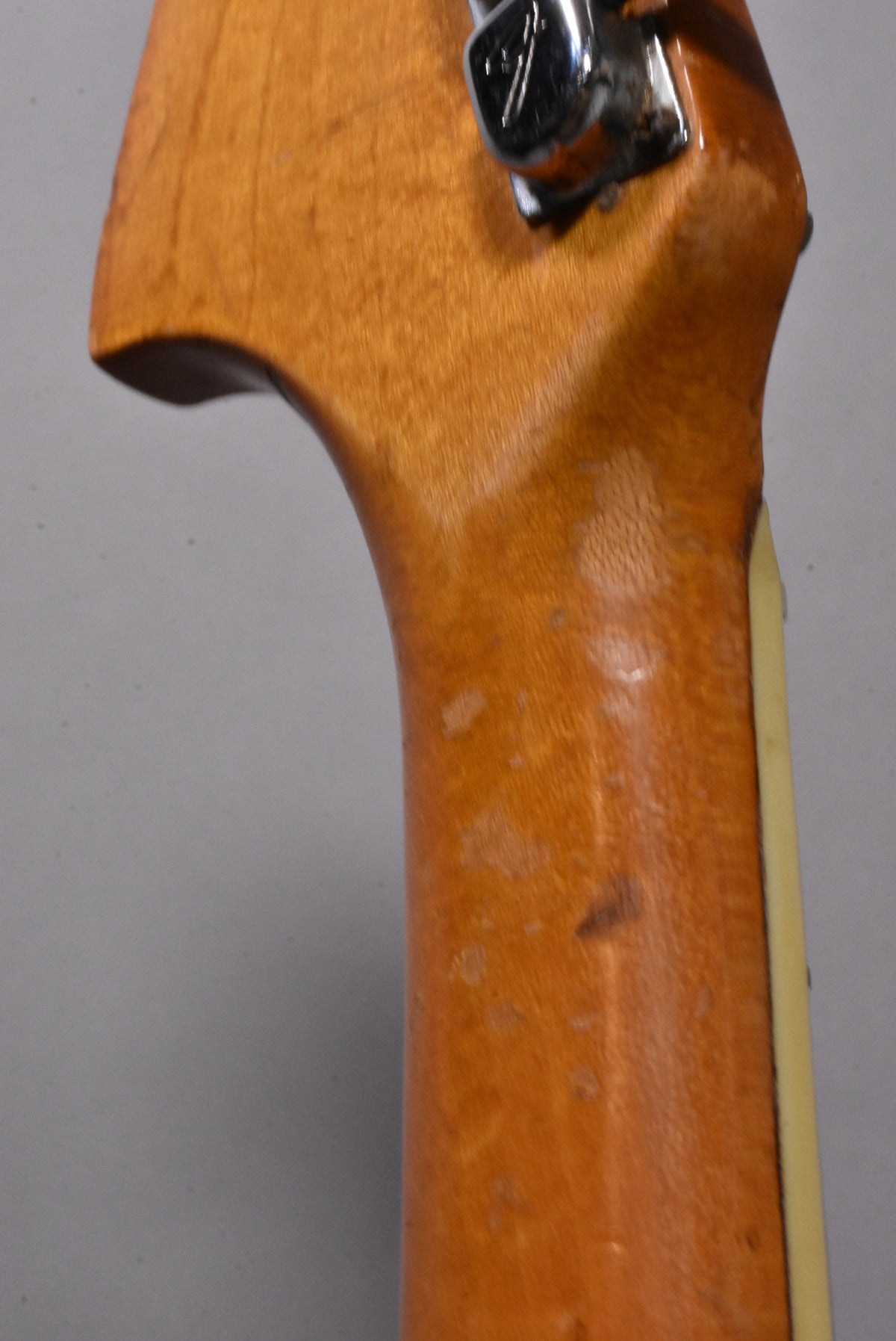 Close-up of the guitar neck's back, showing a worn, ambered finish with several dark spots and a chrome tuning peg.