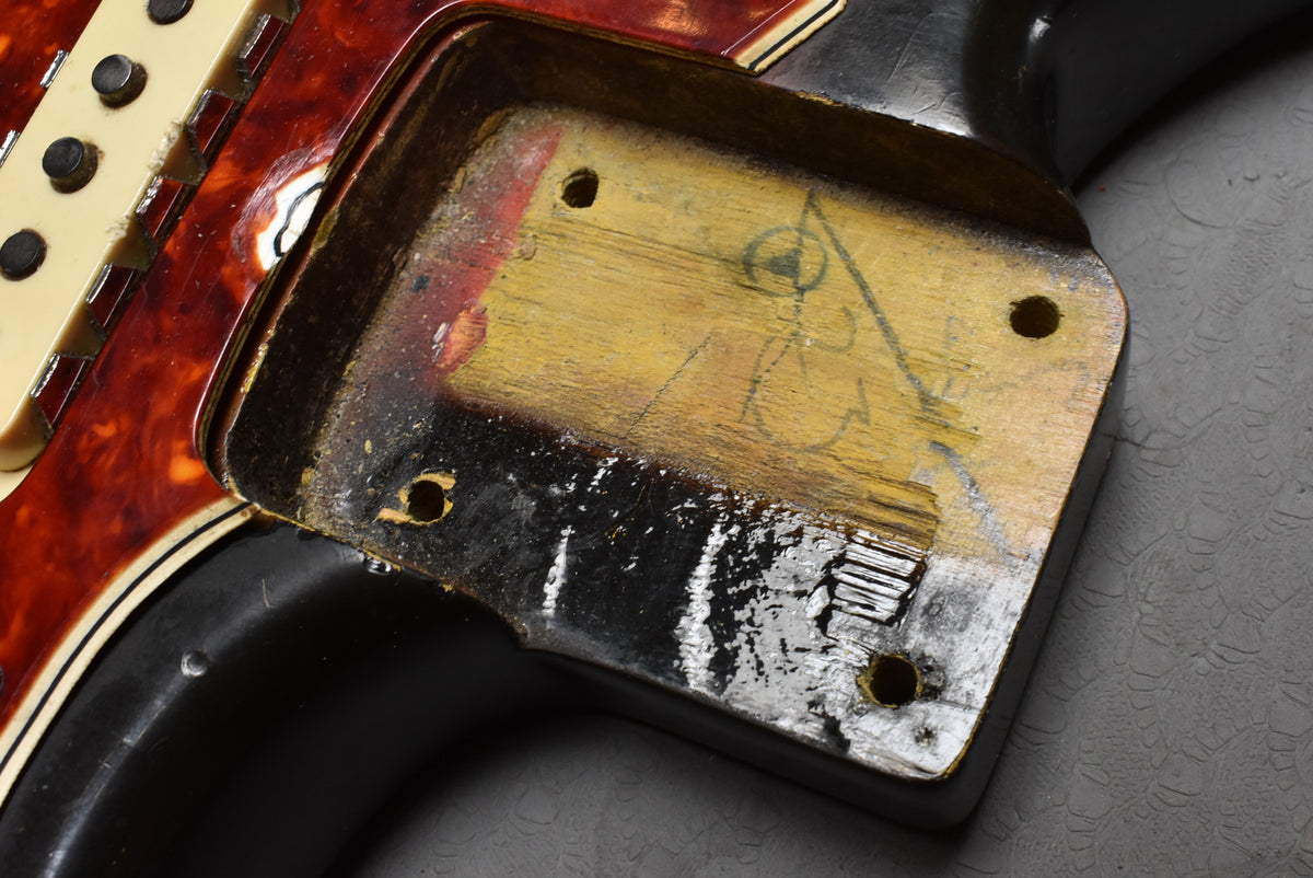 Close-up of the neck pocket, showing worn wood, black finish, and a red tortoiseshell pickguard with cream pickups.