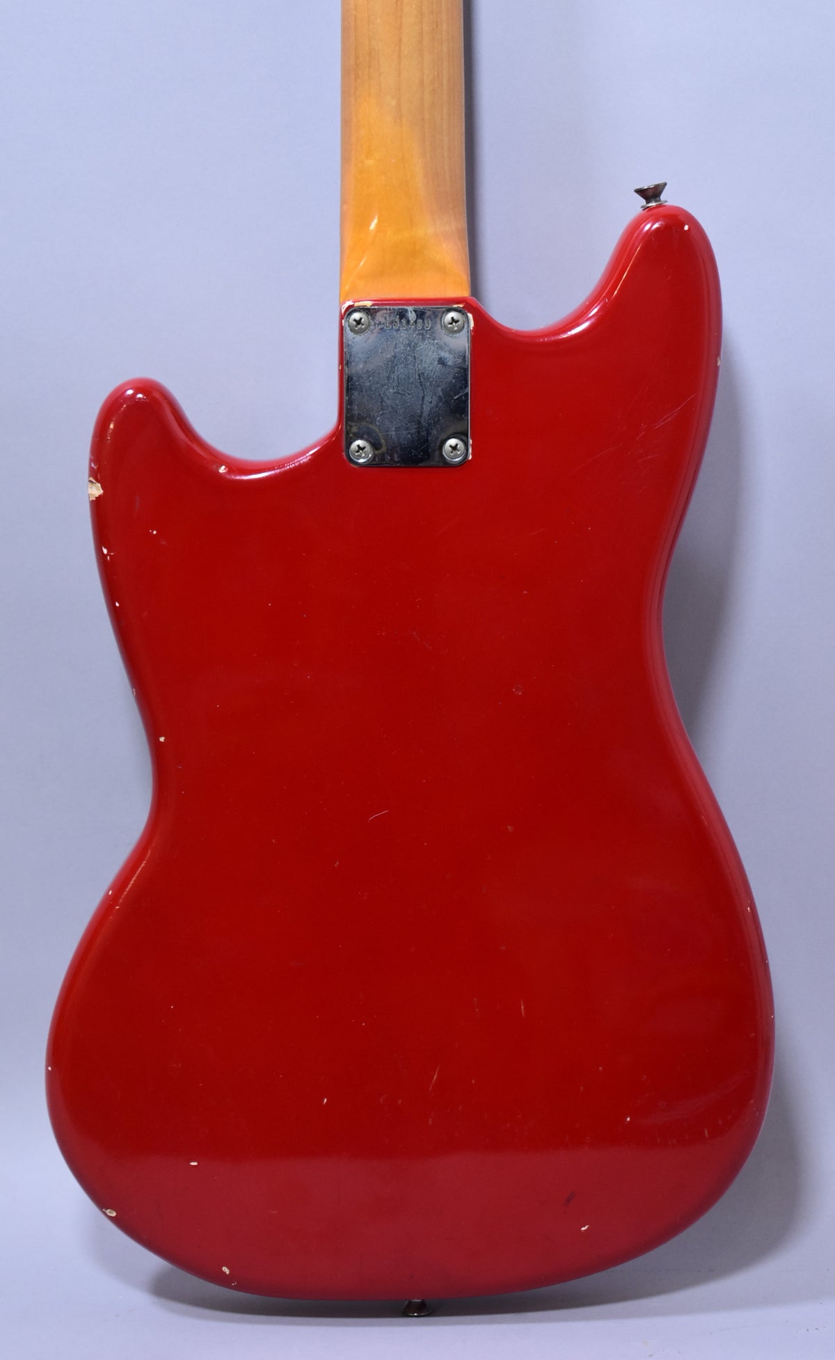 The back of a Dakota Red guitar body with a worn chrome neck plate, a light maple neck, and visible finish chips.
