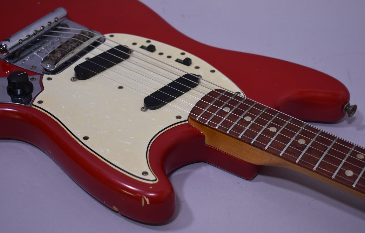Close-up of the red guitar body and neck, showing a pearloid pickguard, two black single-coil pickups, and finish wear near the strap button.