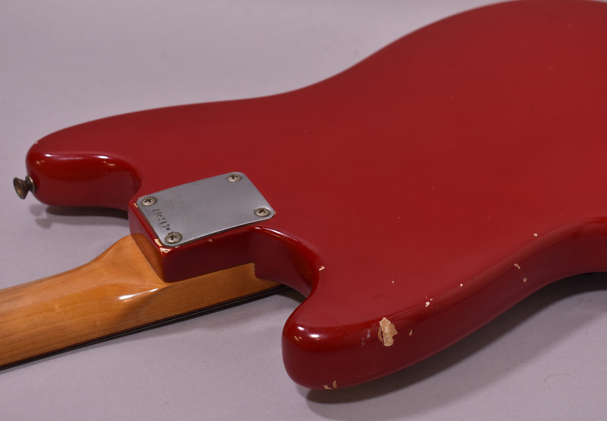 The red guitar body and neck joint are visible from the back, showing a chrome neck plate and significant paint chips on the lower bout.
