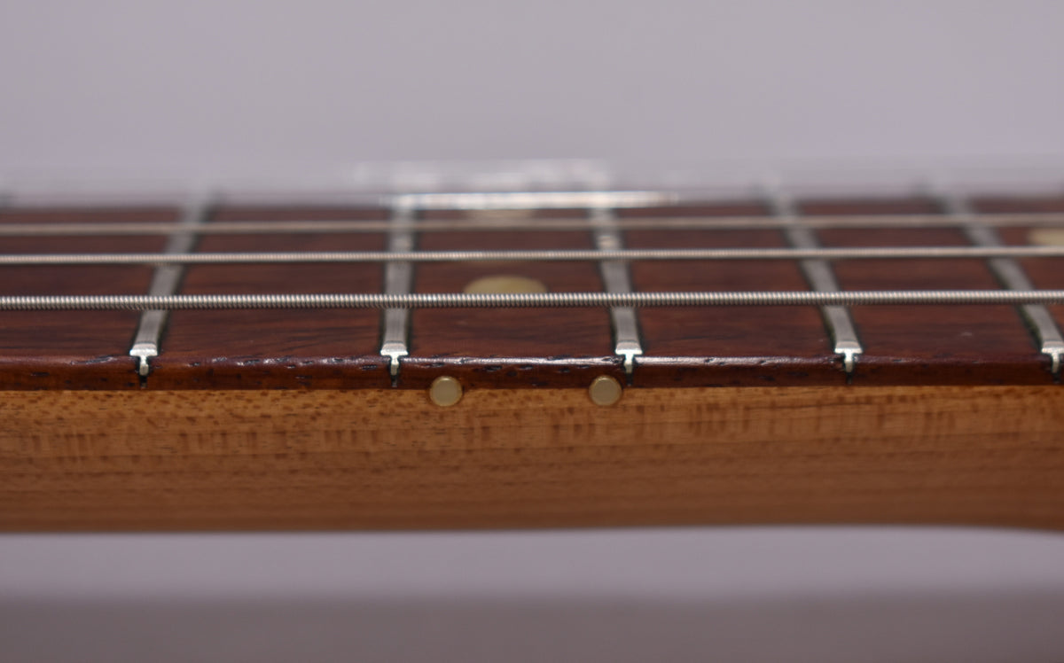 Close-up of the guitar's fretboard and strings, showing two round side dot markers and light wear on the dark wood.