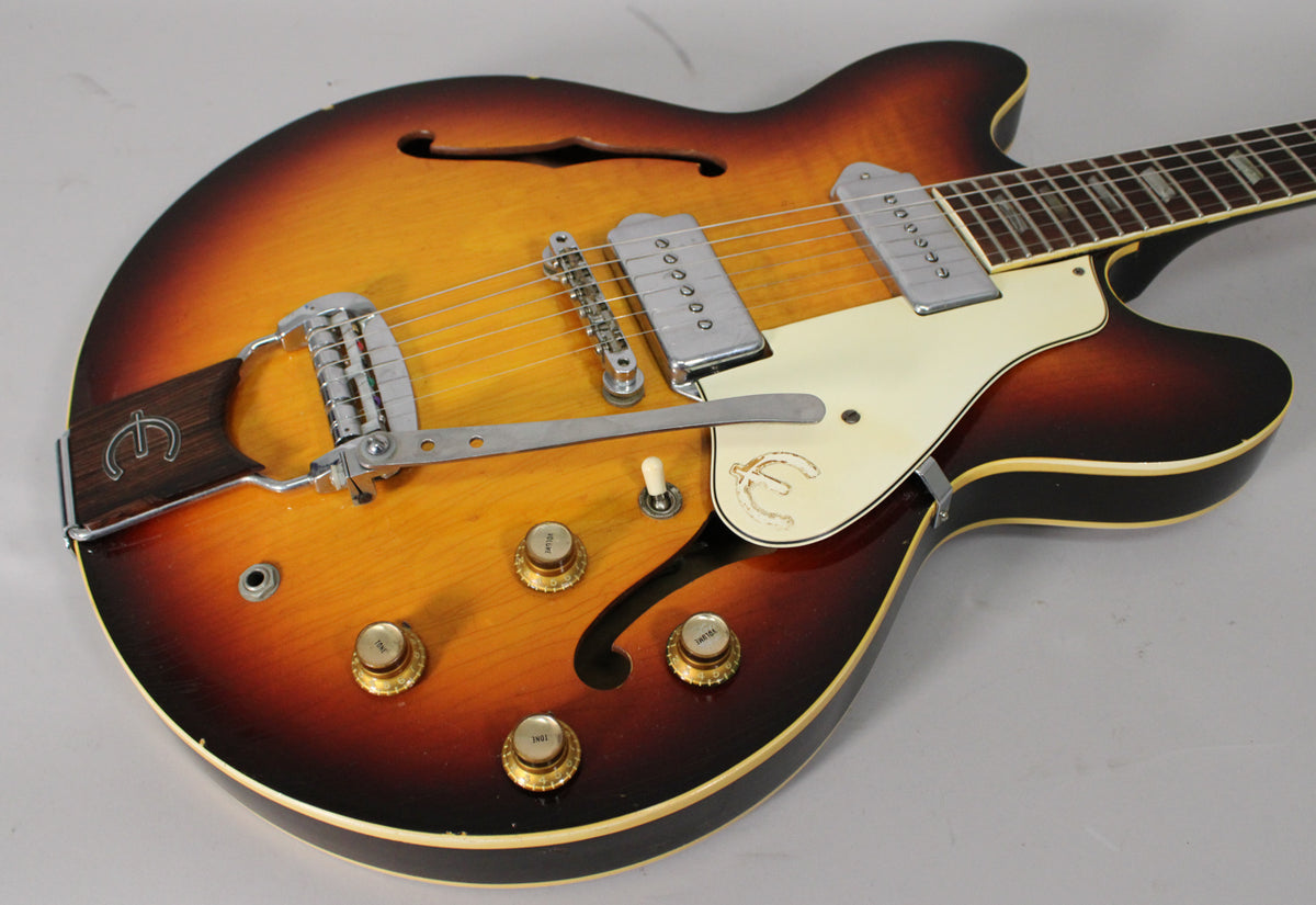 Sunburst archtop electric guitar, angled view of body and lower neck, showing vibrato, two pickups, pickguard, and four gold knobs.