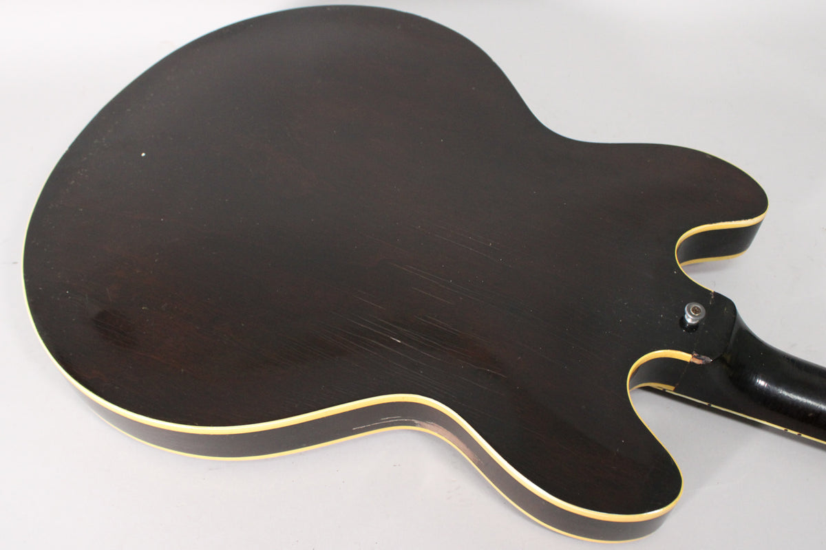 The guitar's dark sunburst back, showing wear and scratches, with cream binding and a neck heel, is angled from the lower bout.