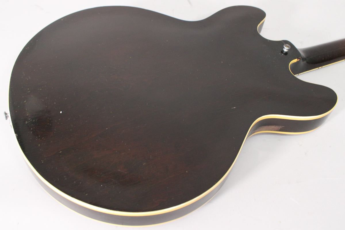 The guitar's dark sunburst back, with visible wear and binding, is angled from the lower bout towards the neck heel.