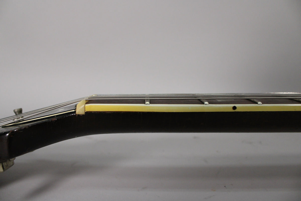 Close-up of the guitar neck from the side, showing the dark brown finish, cream binding, and light wear near the nut.