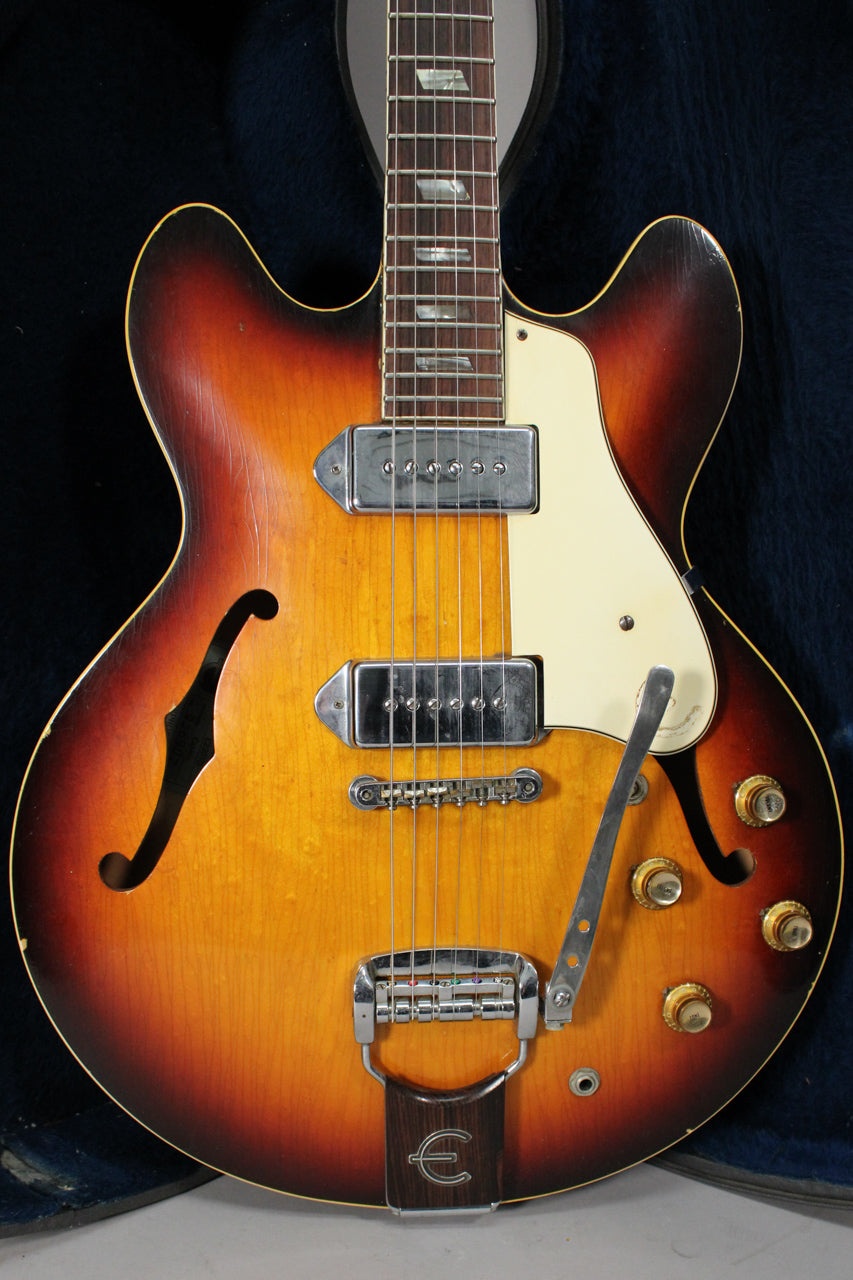 Full-frame view of a sunburst archtop electric guitar with f-holes, two chrome pickups, a vibrato tailpiece, and four gold knobs.