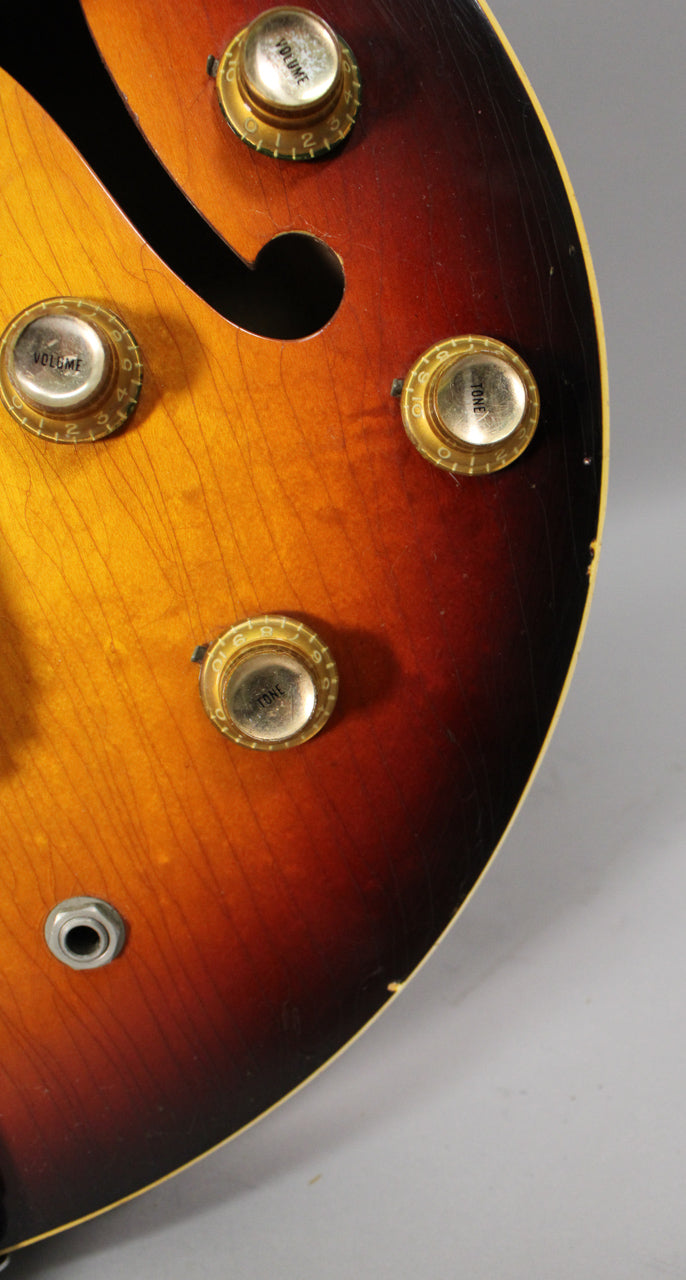 Close-up of the sunburst body, showing four gold-capped knobs, an f-hole, and the input jack, all with visible finish checking.