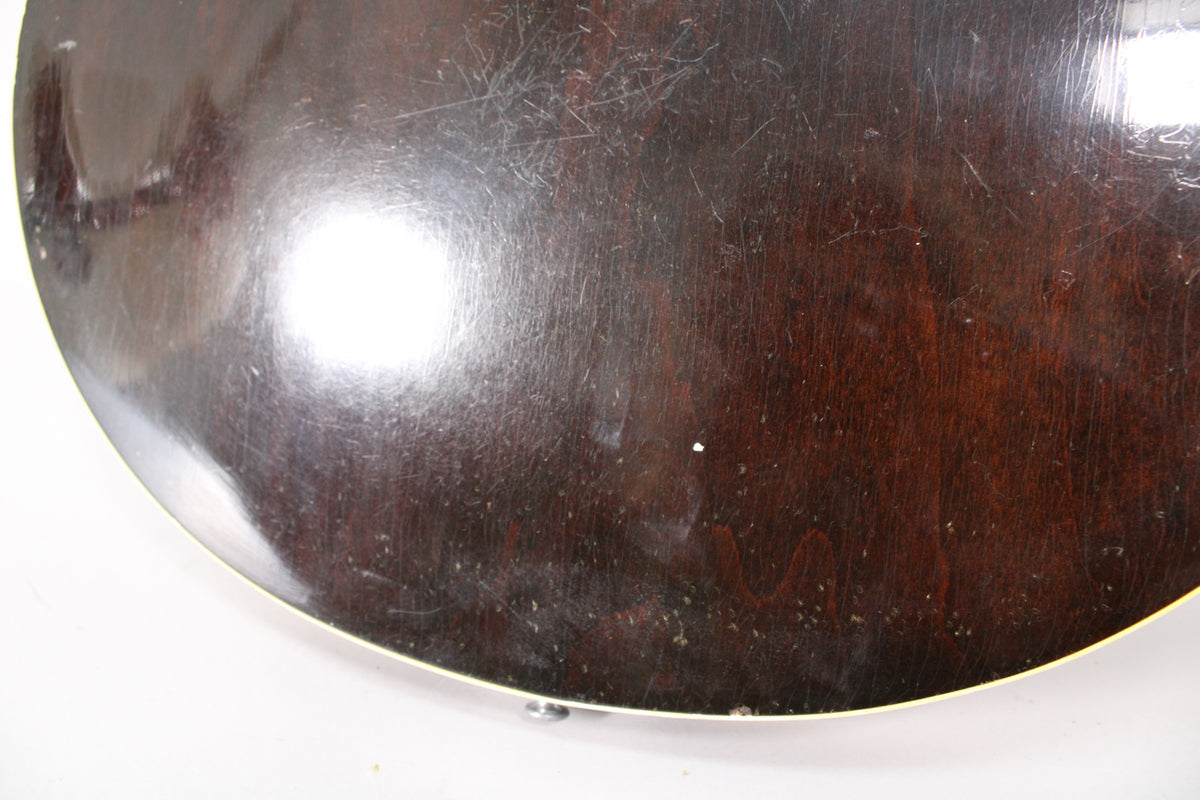 Close-up of the guitar's dark sunburst back, showing extensive surface scratches, dings, and a cream binding along the curved edge.