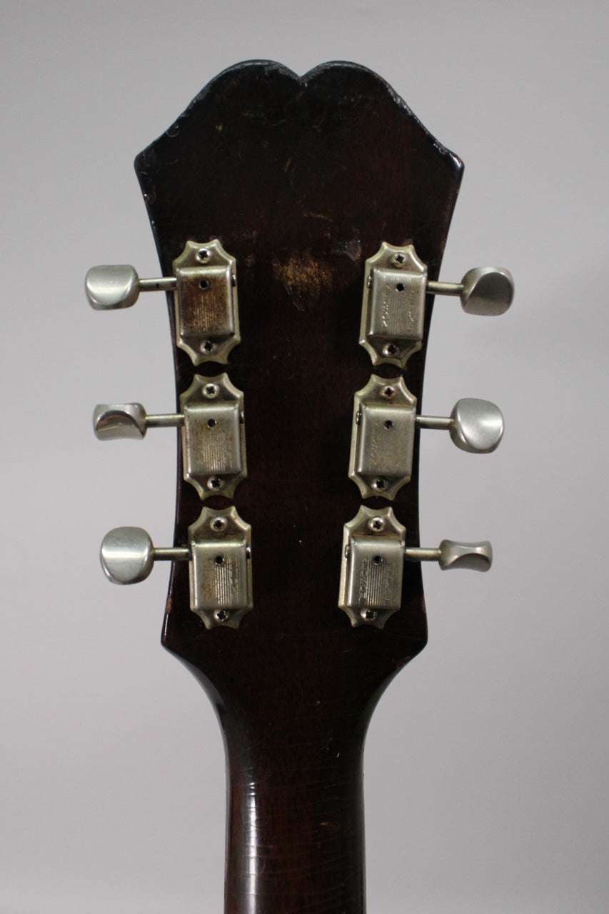 The guitar's dark brown headstock, viewed from behind, shows six aged nickel tuners and notable finish wear and checking.