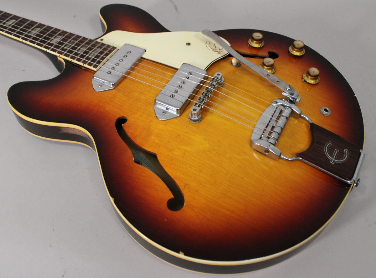 Sunburst archtop electric guitar, angled view of body and neck, showing two P90 pickups, vibrato tailpiece, and four gold knobs.