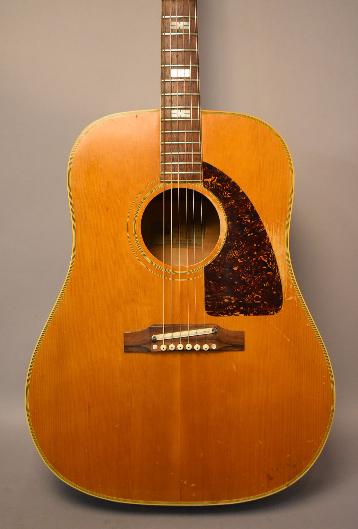 The natural finish acoustic guitar is shown from the front, with a tortoiseshell pickguard, a rosewood bridge, and block inlays on the fretboard.