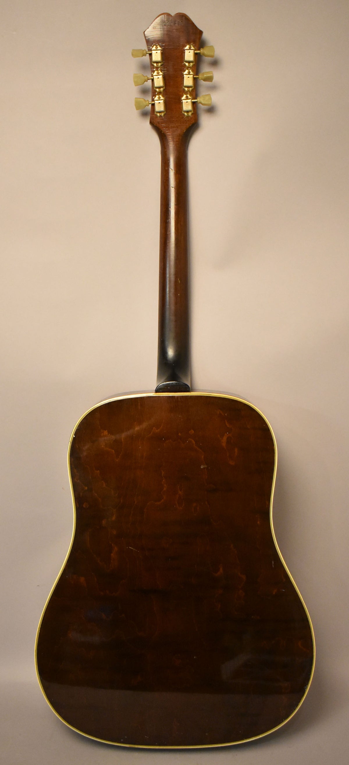The guitar's dark brown back and neck are visible, with six gold tuners and cream buttons on the headstock, showing some wear.