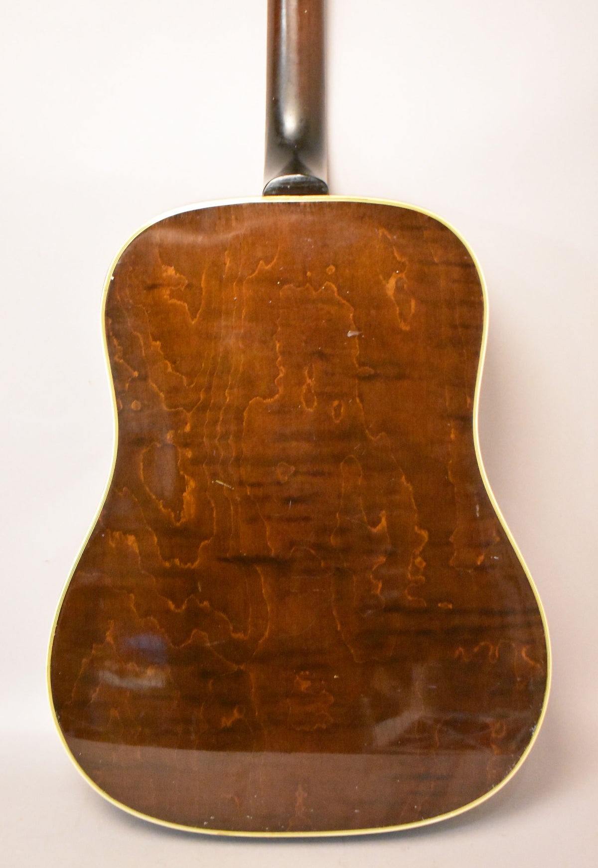The back of the acoustic guitar, showing its dark brown wood grain, light binding, and a few small white scuffs on the glossy finish.